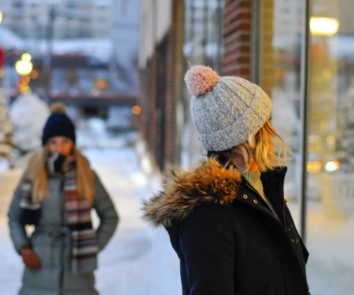 Two woman peering into a store window during the winter.