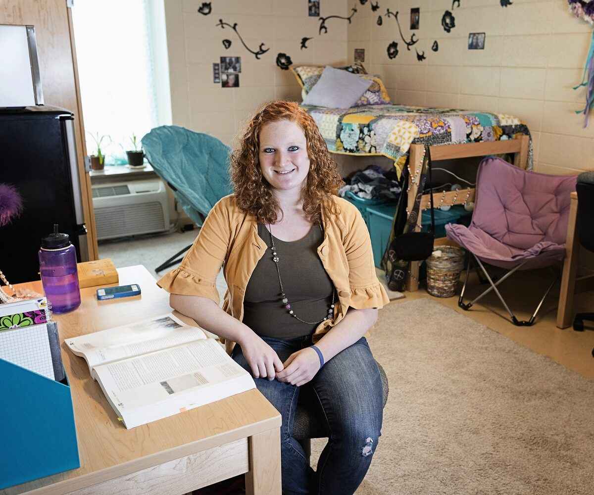 A happy college student sitting in her clean dorm room.