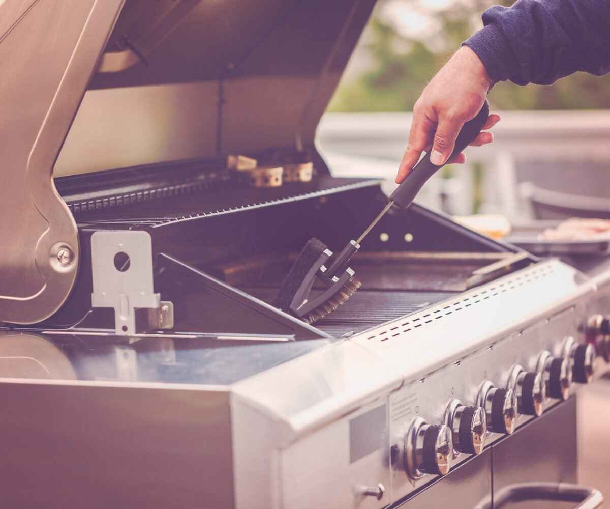 Person cleaning a gas grill with a brush.