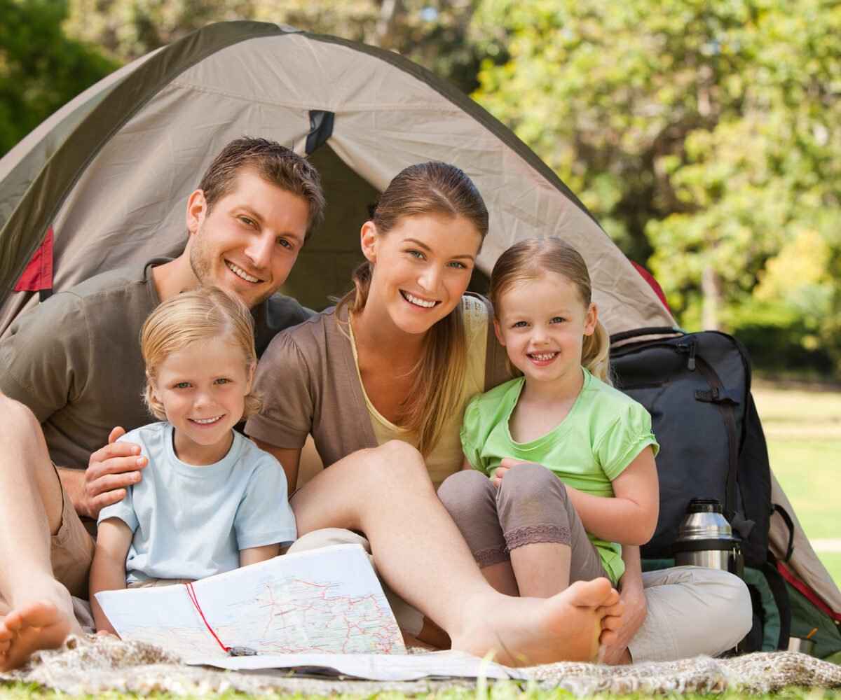 A young family smiling for a photo in front of their camping tent.