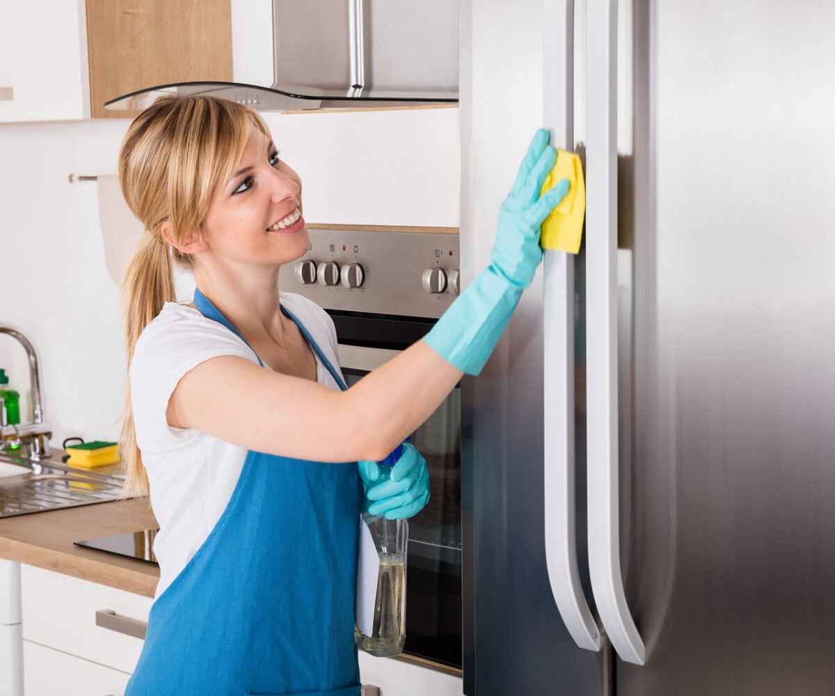A young woman cleaning a refrigerator.