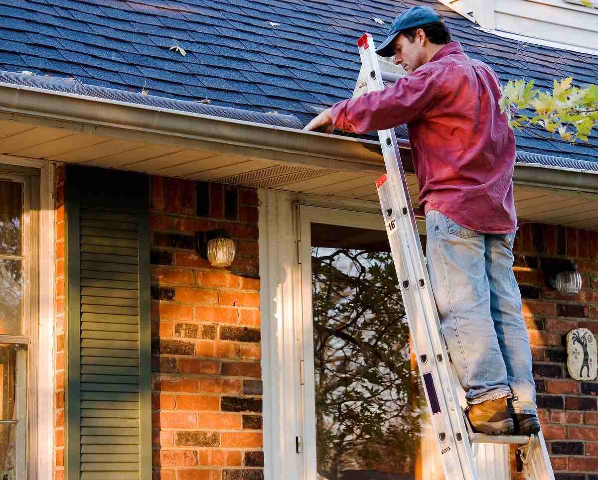 A man standing on a ladder cleaning out gutters.