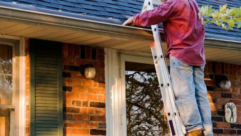 A man standing on a ladder cleaning out gutters.