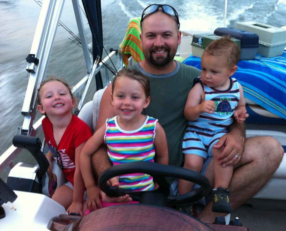 Dad driving boat with three children on his lap.