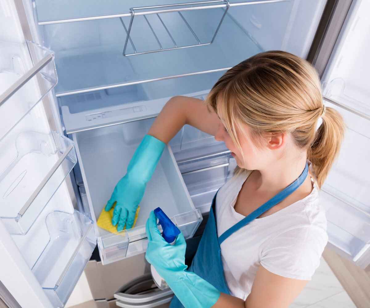 A young woman cleaning the inside of a refrigerator.