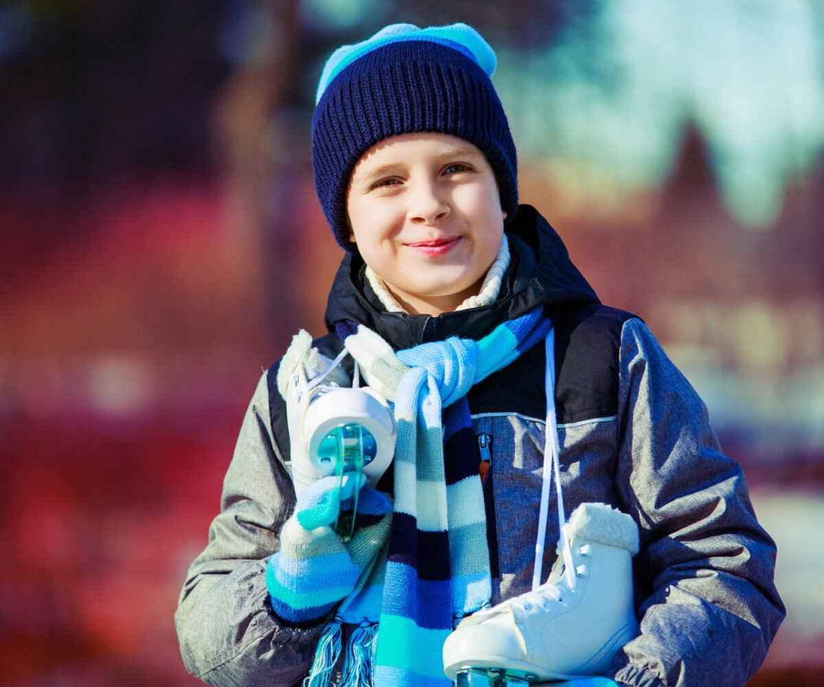 A young boy smiling for the camera with ice skates around his neck.