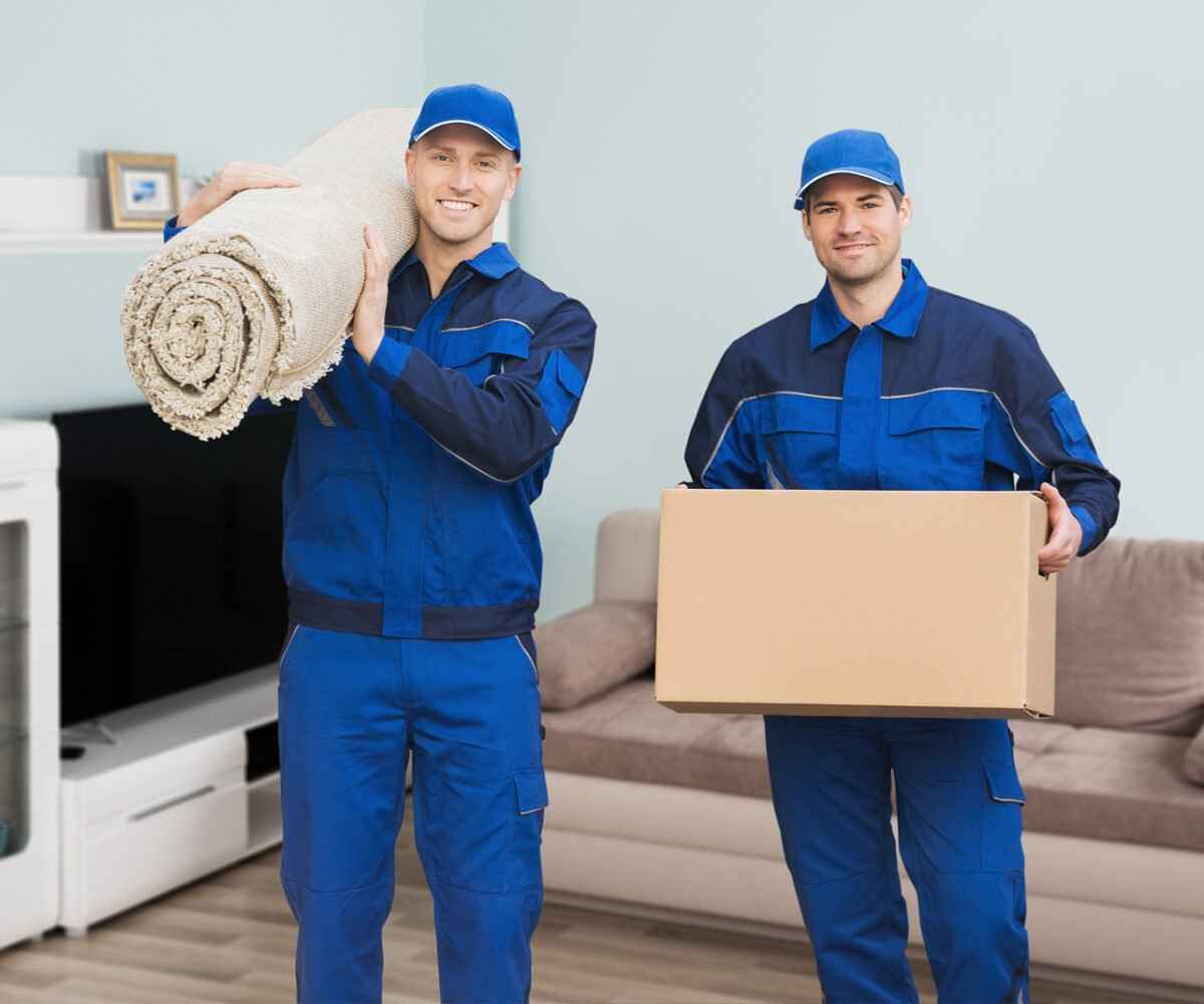 Two movers smiling carrying a rug and moving box.