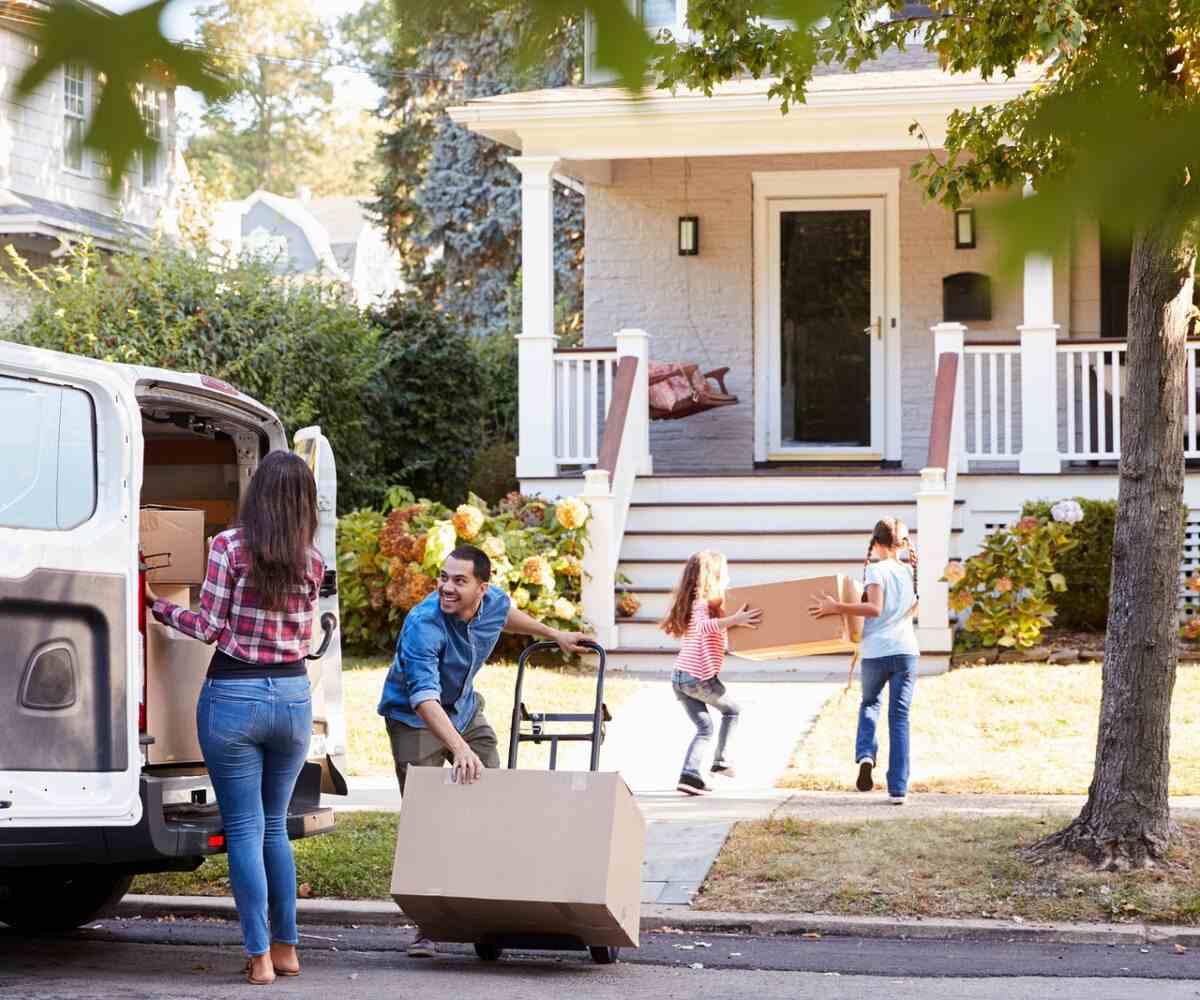 A family moving with children happily unloads boxes into their new home.