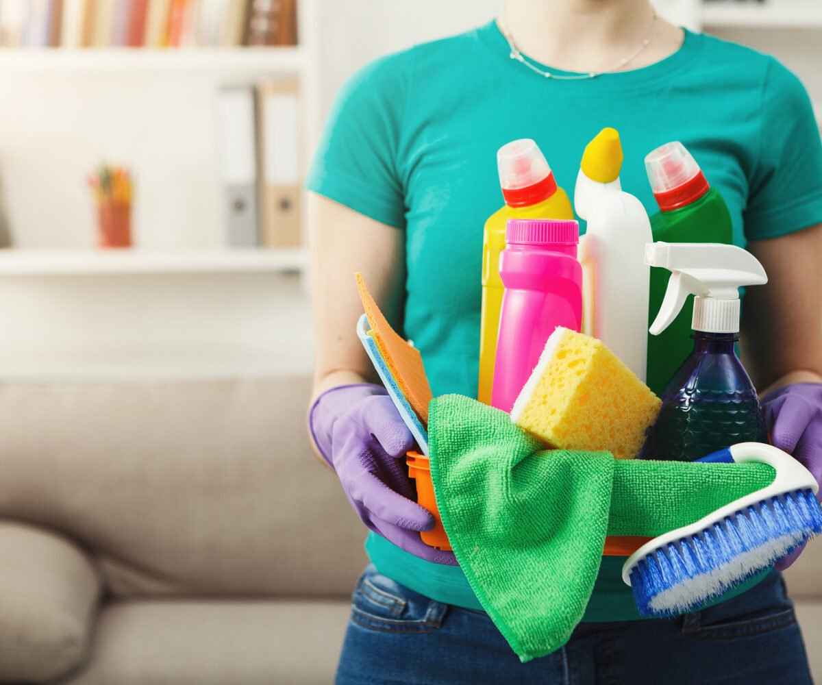 Young woman holding bucket with cleaning supplies.