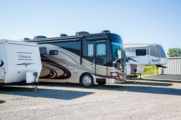 An RV and two trailers parked at a storage facility.