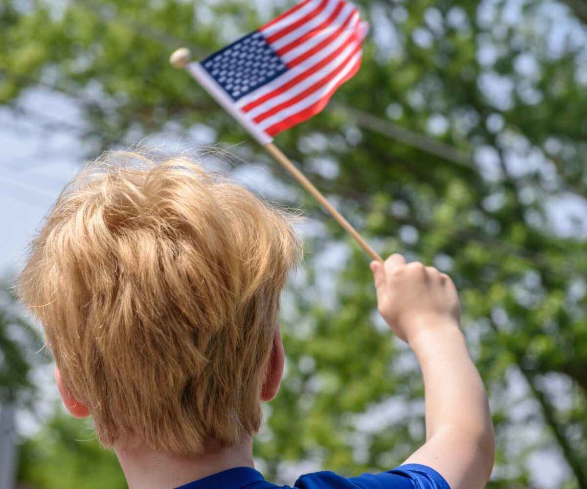 Young boy waving a small American flag in his hands.
