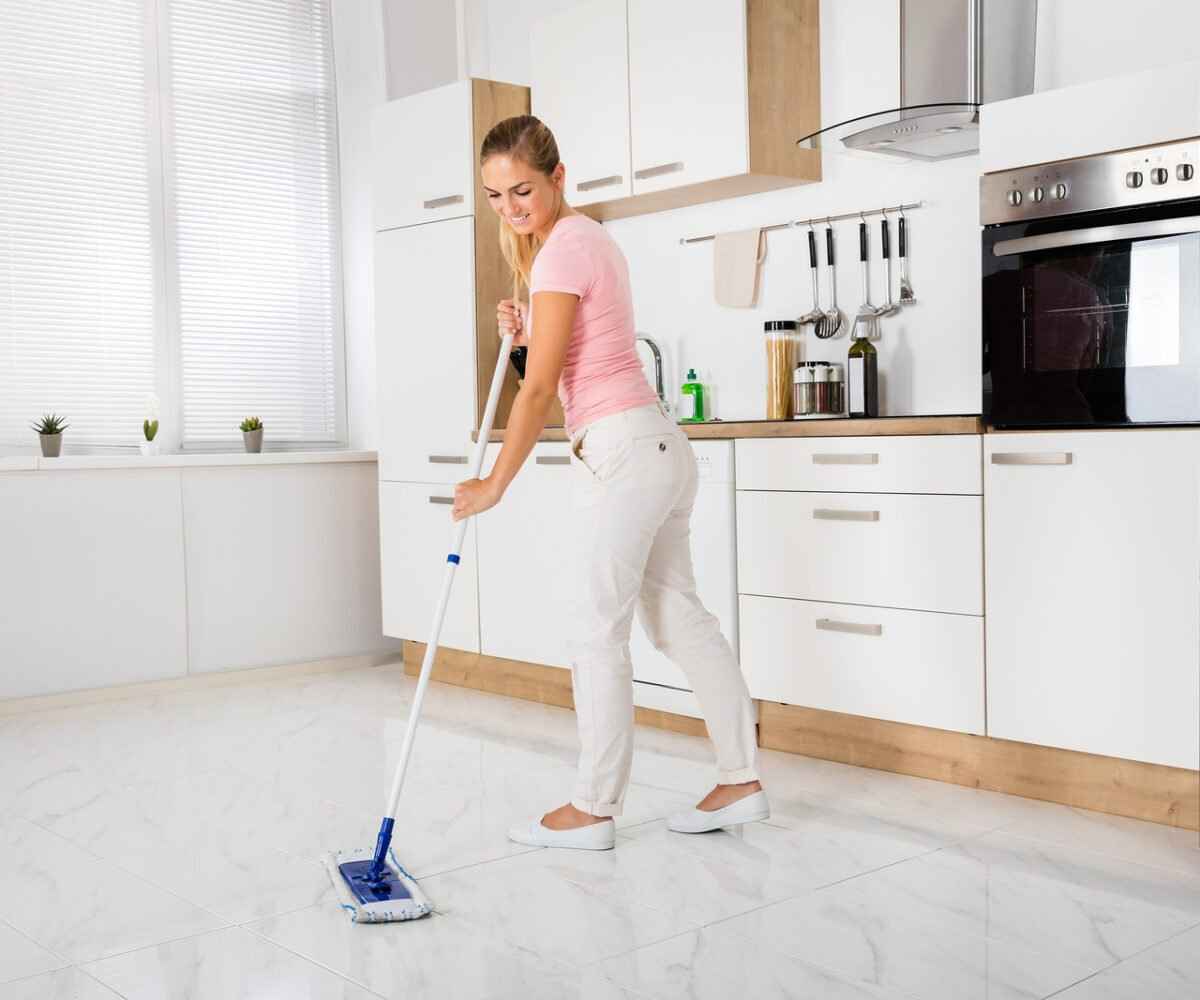 Woman sweeping white tile floors in a clean kitchen.
