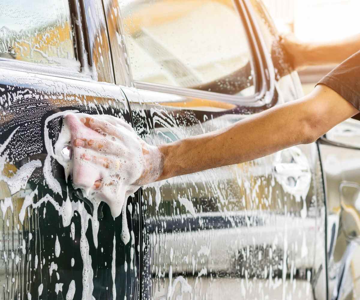 Person washing a black car with soap.