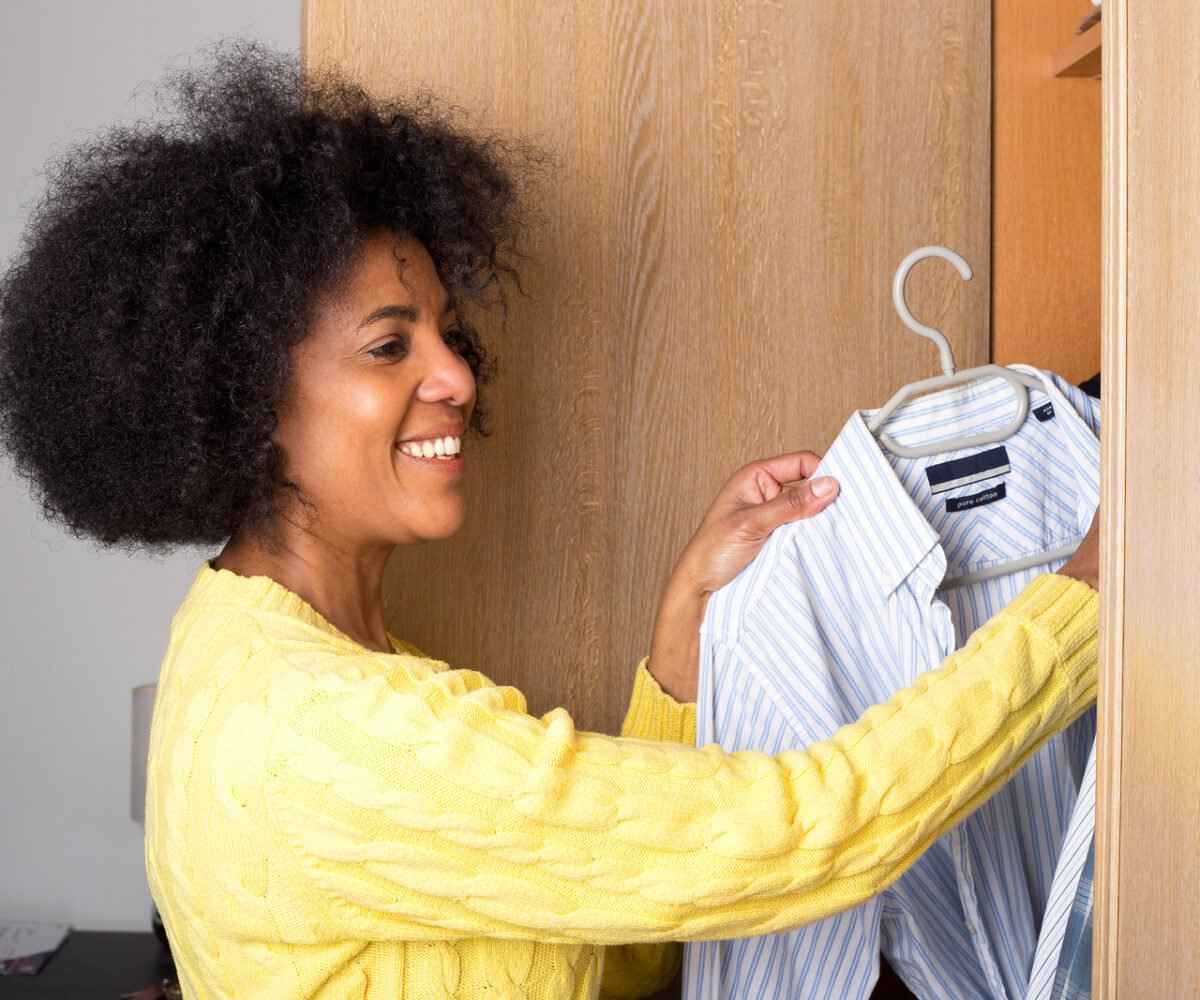 A woman hanging a shirt in a closet.