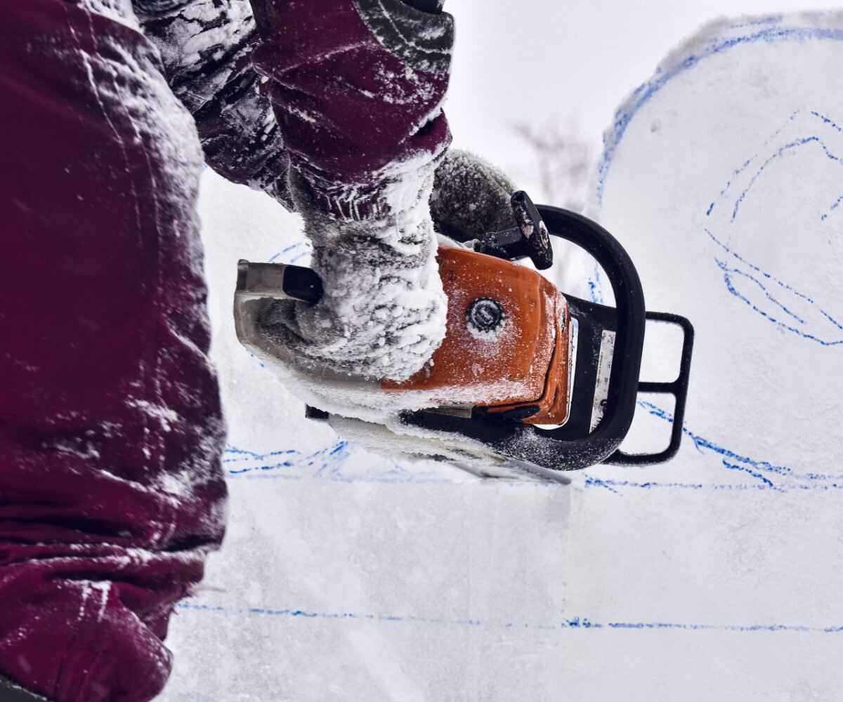 A person carving with a chainsaw in the snow.