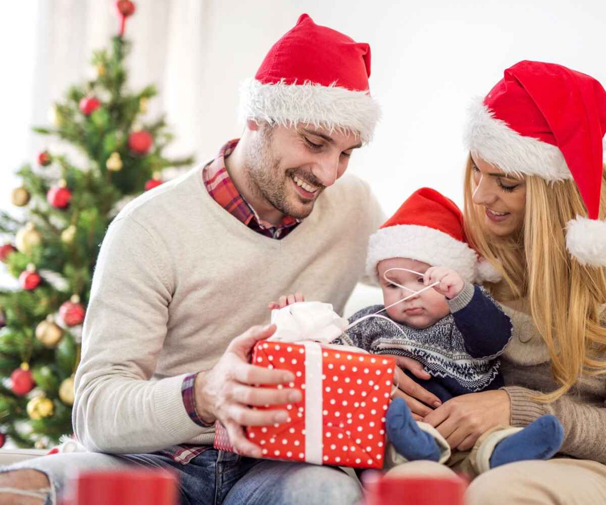 A mom and dad helping their baby open a Christmas present.