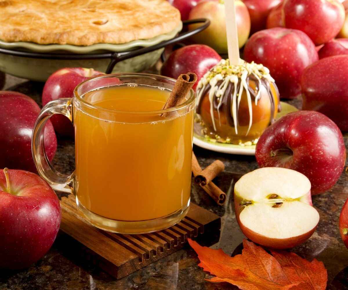 A glass of apple cider surrounded by apples and an apple pie.