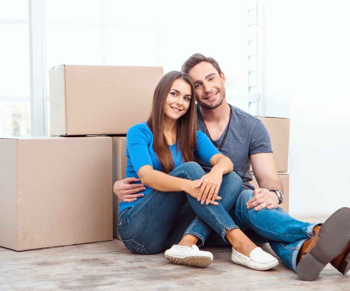 Young couple smiling next to moving boxes.