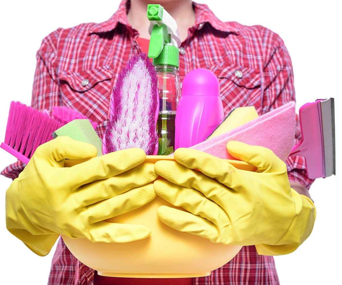 Lady wearing rubber gloves holding a bucket with cleaning supplies.