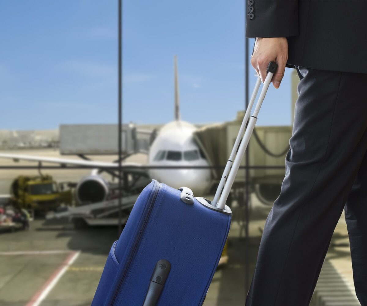 Man in suit rolling suitcase about to board a plane.