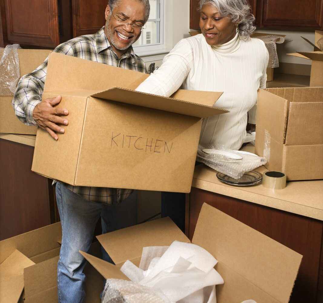 Middle aged couple unloading kitchen supplies from moving boxes.