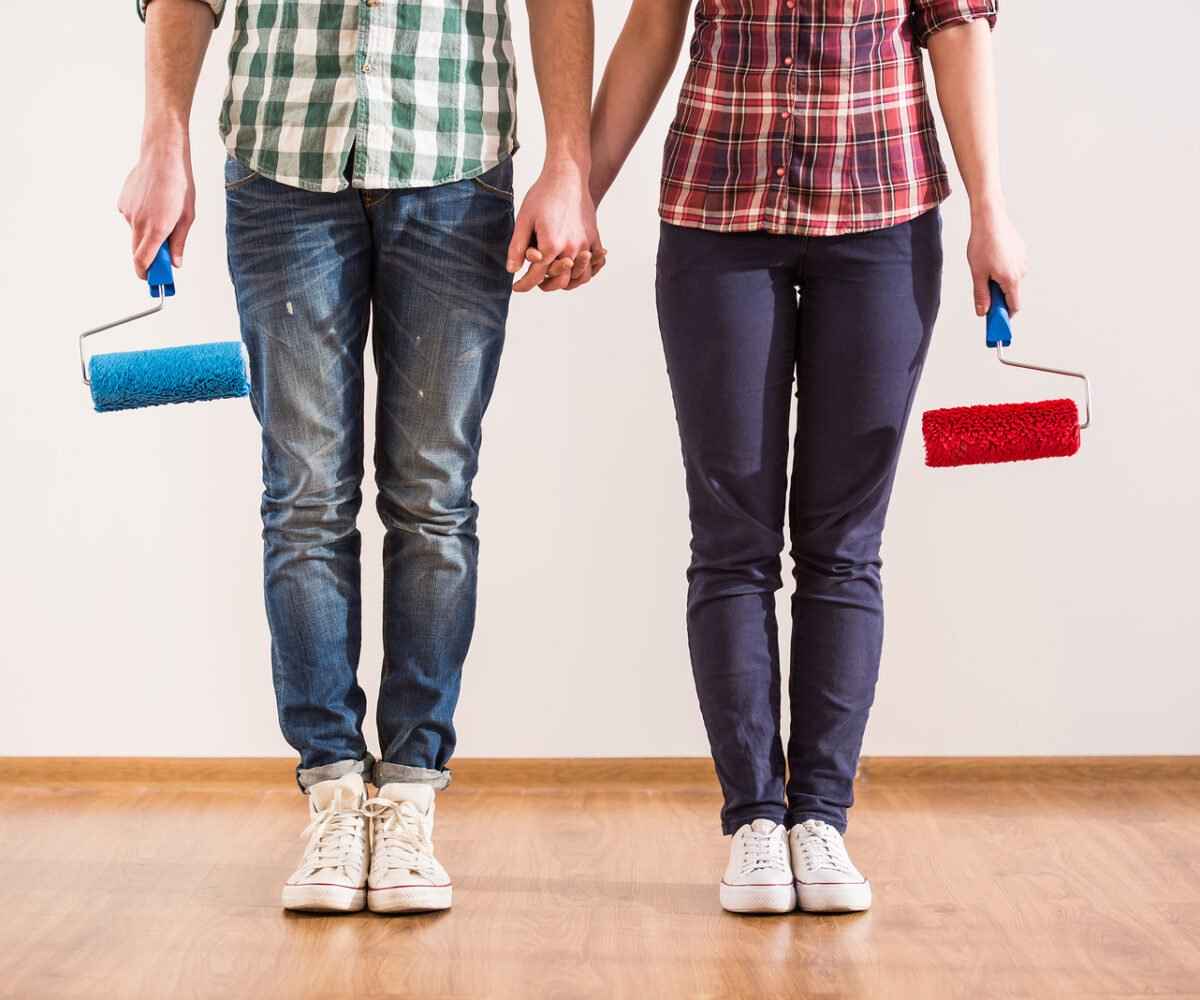 Man and woman holding hands carrying paint rollers.