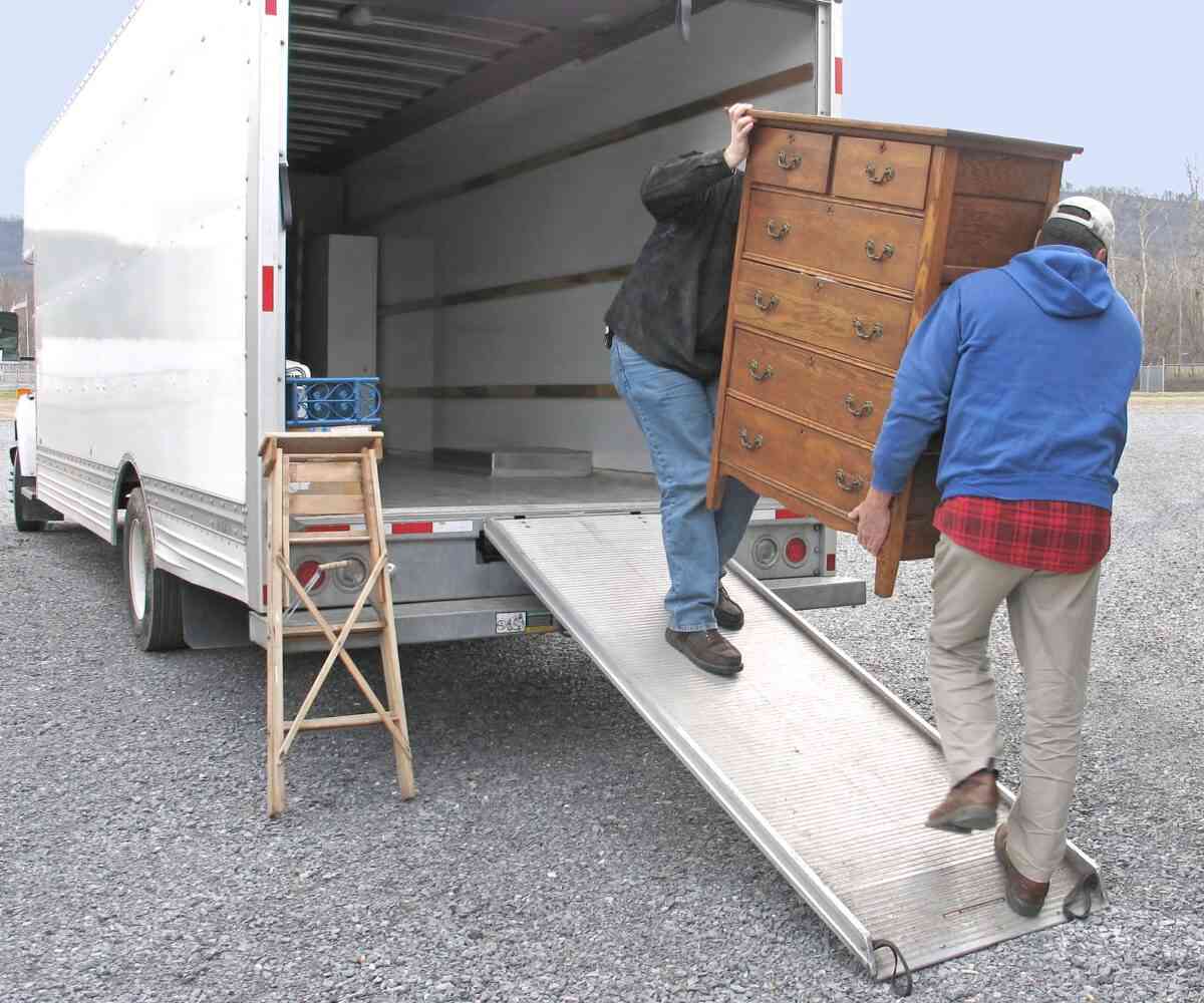 Two men loading a dresser into a moving truck.