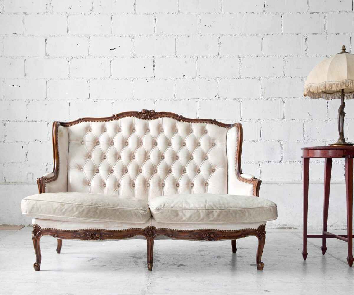 White antique couch next to a side table and lamp.