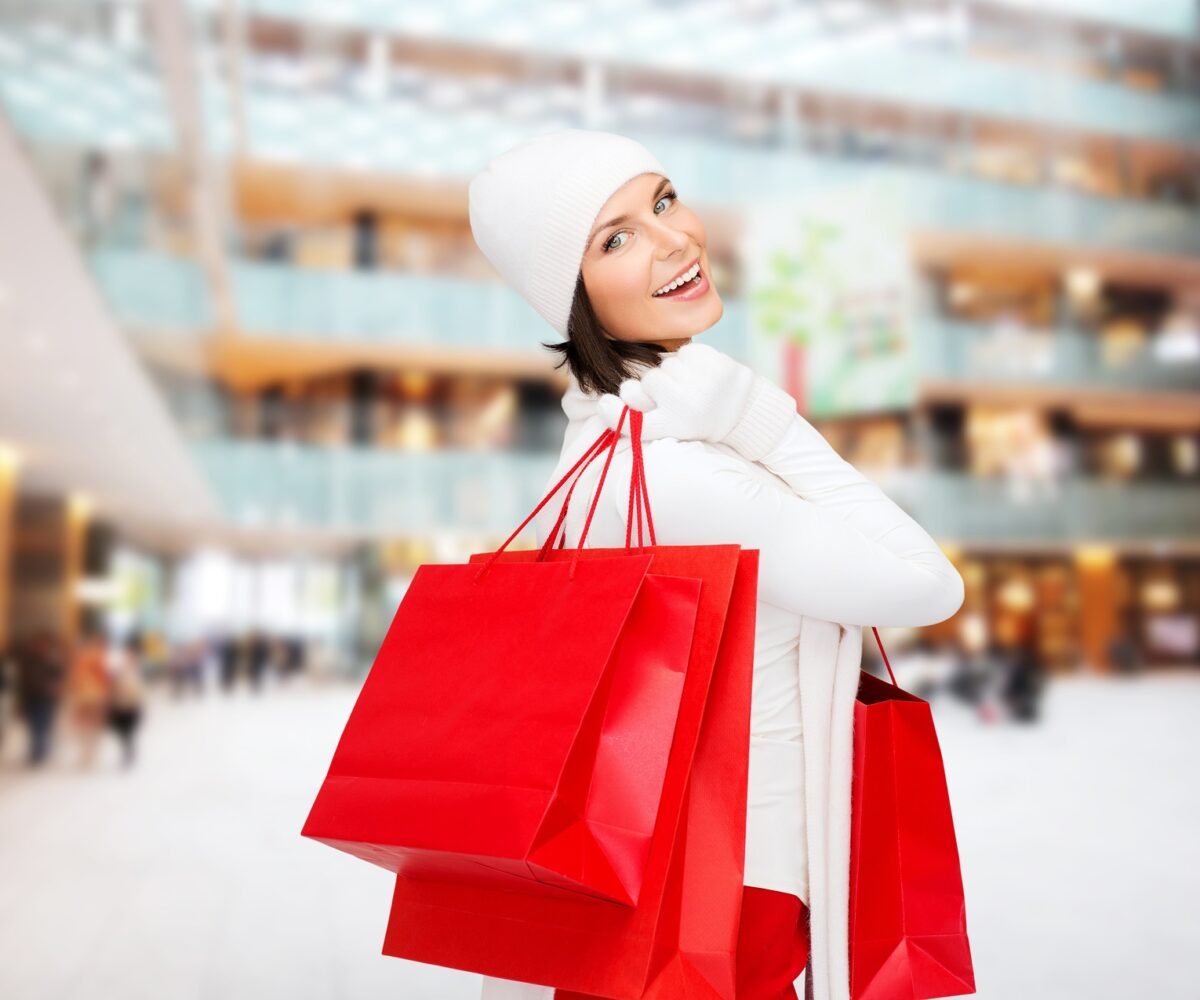 Woman smiling carrying three red shopping bags.