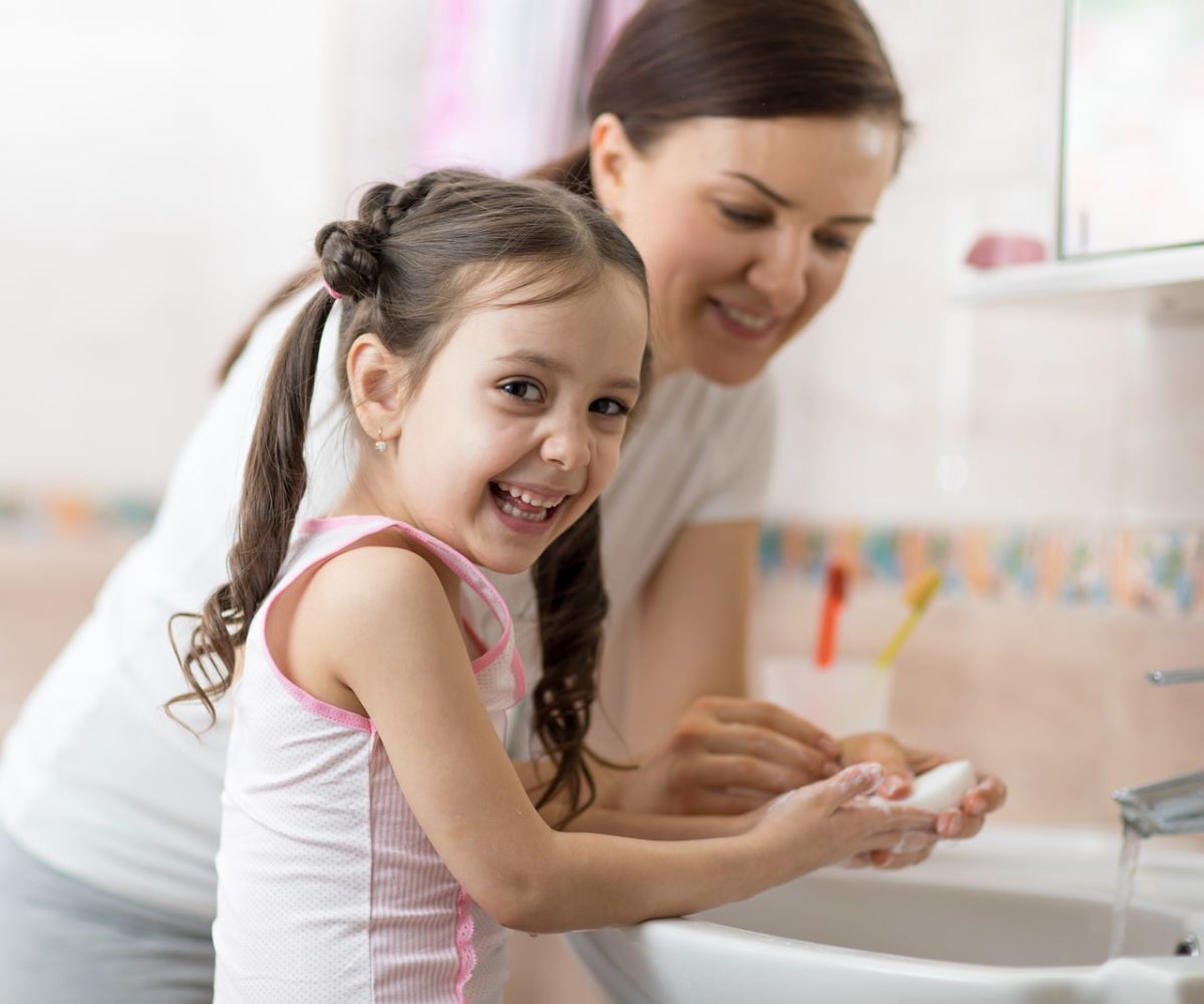 A young girl learning how to wash her hands with her mom.