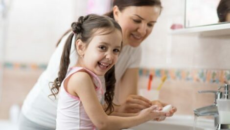 A young girl learning how to wash her hands with her mom.