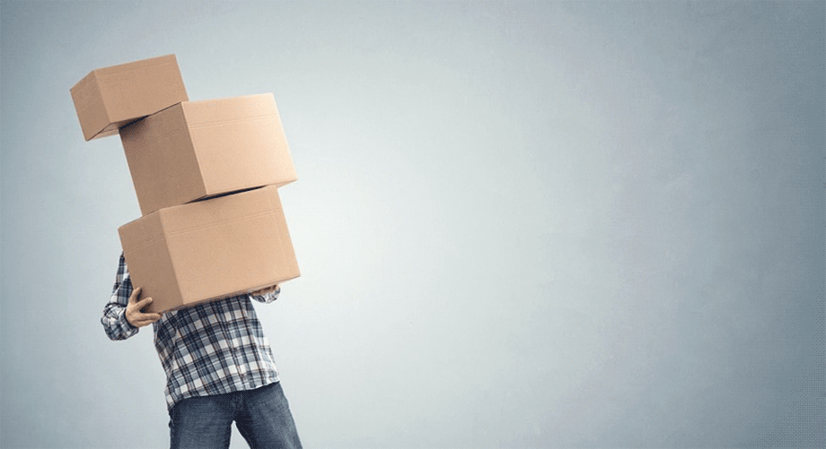 Man struggling to carry three stacked moving boxes.