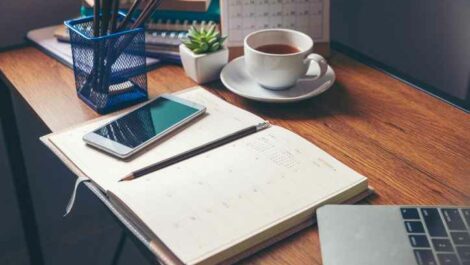 Calendar, pens, coffee, and smartphone sitting organized on a home office desk.