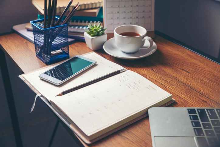 Calendar, pens, coffee, and smartphone sitting organized on a home office desk.
