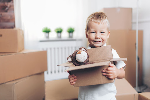 A smiling toddler that is packing toys surrounded by moving boxes.