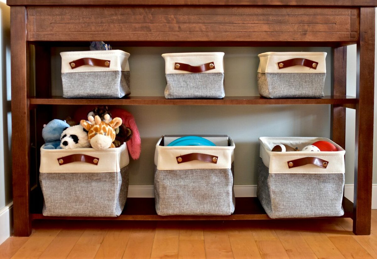 A waist-high wooden table is set against a blue wall with two shelves below it that hold bins storing various items like chew toys and sporting equipment.